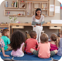 Children sitting on the floor, attentively listening to a story being read by a teacher at Little Lights.